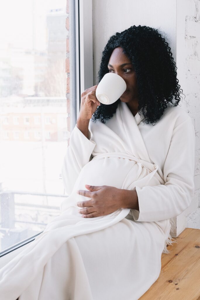 Pregnant woman drinking coffee while holding her baby bump