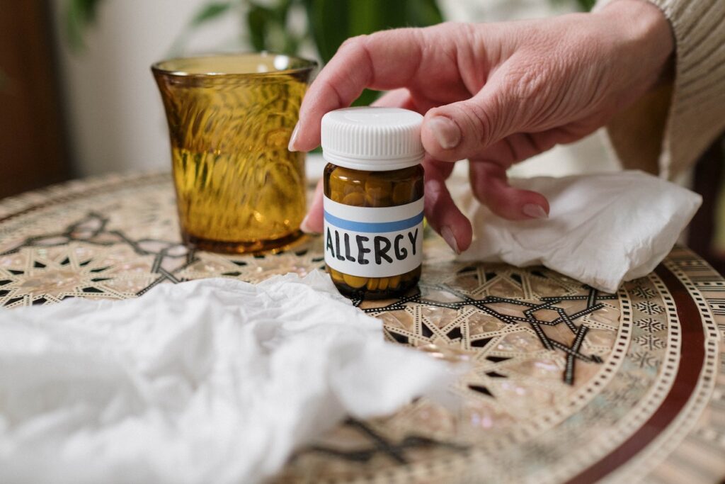 Une main tient un flacon de médicament posé sur une table avec l'inscription "allergie" en anglais